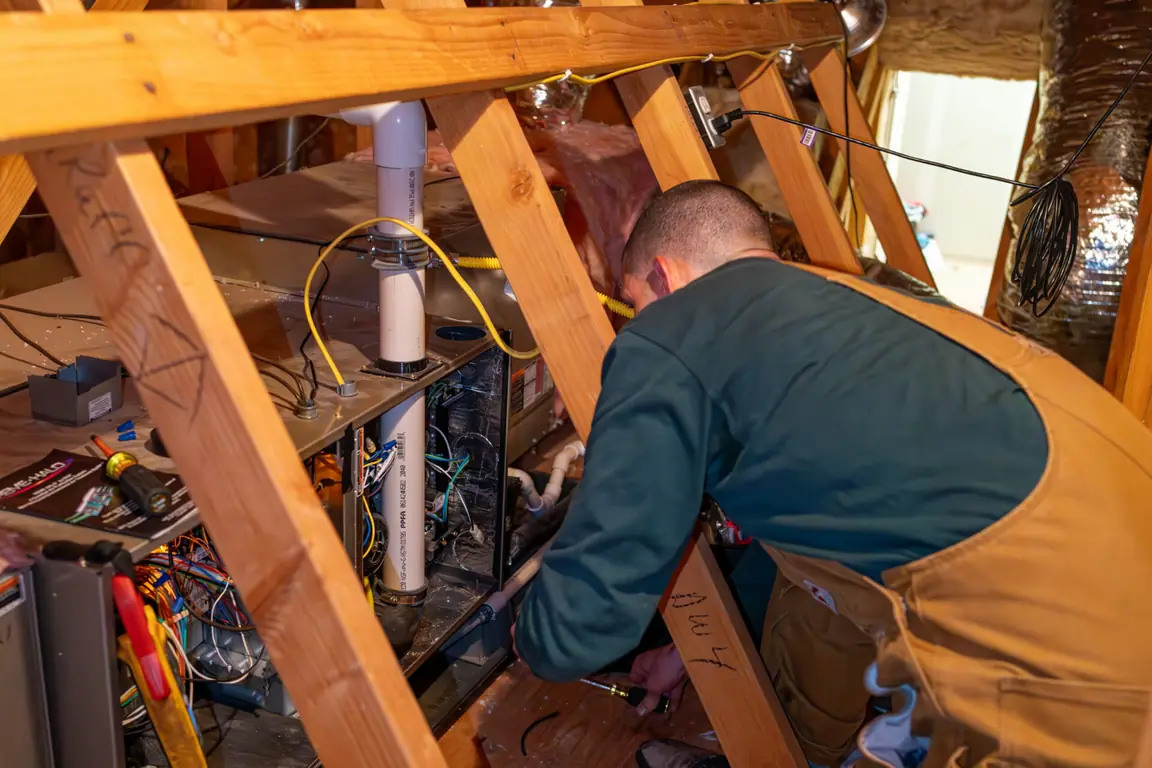 Technician inspecting an older furnace in a Bandon attic to evaluate repair or replacement options.